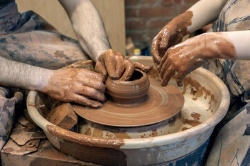 hands of a master potter and a child making dishes. A lesson in a pottery workshop. hands of a potter, creating an earthen jar on the circle