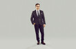 Young attractive Caucasian man in glasses with smile looks at camera posing for picture in business suit manager or trader dressed in strict dark suit stands in gray studio. Career, entrepreneurship