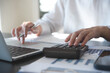© tippapatt - Close up of business woman accountant hand using calculator and laptop computer for calculating finance on desk office. business financial accounting concept