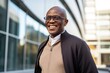 © Anne Schaum - Portrait photography of a happy Nigerian black man in his 50s wearing a chic cardigan against a modern architectural background
