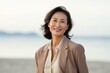 © Robert MEYNER - Portrait of mature Asian businesswoman smiling at camera while standing on beach
