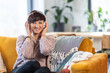 © leszekglasner - Smiling woman listening music on wireless headphones on sofa at home