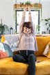 © leszekglasner - Cheerful woman stretching on sofa at home looking at camera