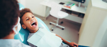 An African-American Child Sitting In A Dental Clinic Chair With Their Mouth Open, Waiting For The Dentist To Perform An Oral Inspection, Copy Space