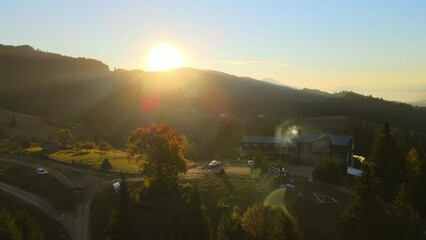 Wall Mural - Wooded hills of Carpathian mountains in Ukraine with small traditional village houses at sunset. Brightly illuminated with setting sun evergreen woods with scattered local homes at fall season