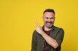 A smiled handsome senior man pointing index finger up isolated over yellow background dressed in green shirt and brown t-shirt