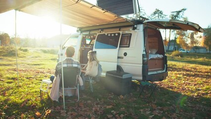 young couple enjoying beautiful sunset having picnic in the forest near the camping bus. traveling p