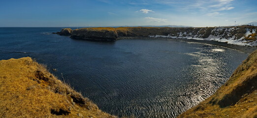 Wall Mural - Russia. Kuril Islands. Panorama of the high steep coast of the Sea of Okhotsk on the island of Iturup at the foot of snow-capped volcanoes.