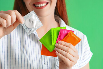 Wall Mural - Young woman with condoms on green background, closeup