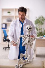 Wall Mural - Young male doctor with skeleton in the clinic
