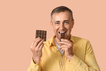 Canvas Print - Mature man eating tasty chocolate on beige background, closeup