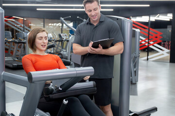 Coach man guidance workout with legs muscles stretch with equipment machine with woman in fitness gym club, strength and flexibility training, woman exercise with instructor or trainer, sport concept.