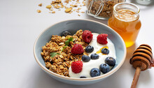 Healthy breakfast. Granola, muesli with pumpkin seeds, honey, yogurt and fresh berries in a ceramic bowl with a cup of coffee on white background.