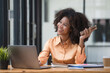© Songsak C - Portrait of a beautiful confident businesswoman using a laptop computer holding a mobile phone sitting in a modern office. Smiling African American freelancer working online from home.