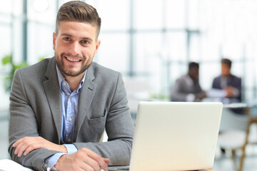 Wall Mural - Portrait of a cheerful young businesswoman sitting at the table in office and looking at camera.