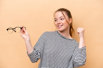 Canvas Print - Young caucasian girl with glasses isolated on beige background celebrating a victory