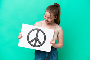 Canvas Print - Young caucasian woman isolated on green background holding a placard with peace symbol