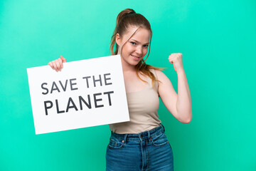 Wall Mural - Young caucasian woman isolated on green background holding a placard with text Save the Planet and doing strong gesture