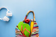 Eine bunte Strandtasche gepackt mit Flipflops, einer Trinkflasche und einem Apfel. Blauer Hintergrund, Draufsicht.