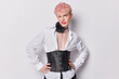 Indoor shot of pink haired transgender man wears elegant attire which perfectly complements his expressive personality winks eye has flirty expression keeps arms on waist isolated on white background
