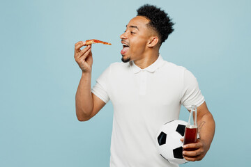 Young excited happy man fan wear basic t-shirt cheer up support football sport team hold in hand soccer ball eat pizza drink beer watch tv live stream isolated on plain pastel blue color background.