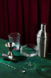 Champagne glass, shaker, cocktail mixing spoon and jigger on dark green table