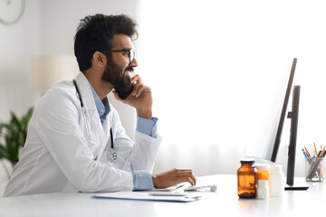 Arab doctor working at clinic, using computer, have phone conversation