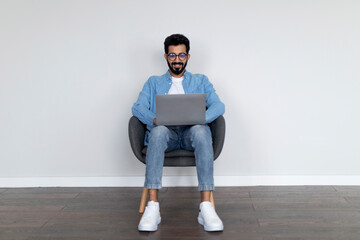 Indian Male Freelancer With Laptop Working Online, Sitting In Chair At Home