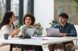 © Prostock-studio - Three colleagues of mixed ethnicity sitting at table in office