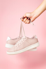 Wall Mural - Fenale Hand with stylized fingernails holding hanging pink sneakers by the laces on white background. Hand with a new sport shoe.