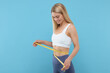 © New Africa - Slim woman measuring waist with tape on light blue background. Weight loss