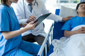 Two doctors caring for a patient lying in a bed in a hospital room with two nurses, a healthcare worker giving support and consulting a patient in bed