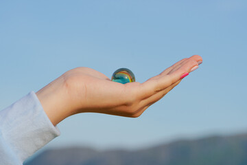 Close-up of child's hand holding in her open palm small glass ball against sky