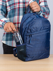 Close-up of a young male student taking out a bottle of water from his backpack.