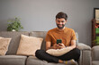 © IndiaPix - Young man using mobile phone while relaxing on sofa in living room