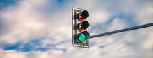 A Traffic Light With A Green Light On A Background Of A Blue Sky With White Clouds. Banner