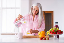Mature Woman Pouring Detox Water In Glass At Home