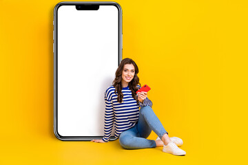 Sticker - Full size photo of positive girl sit floor use telephone empty space poster isolated on yellow color background