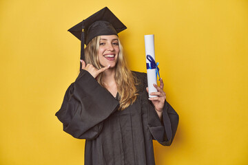 Young caucasian woman wearing a graduation robe holding a diploma Yshowing a mobile phone call gesture with fingers.