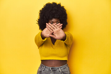 African-American woman with afro, studio yellow background doing a denial gesture