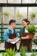 © Drobot Dean - Man writing down notes in clipboard while woman florist teaching him to handle with plants in greenhouse