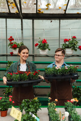 Wall Mural - Beautiful woman and man with down syndrome smiling at camera while working in greenhouse