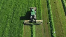 Modern Tractor Machine With Mower Mows Fresh Green Grass For Sillage, Livestock Feed Or Hay. Farmer Work On Agricultural Field. Tractor On Autopilot Driving Along Vertical Straight Line. Aerial View
