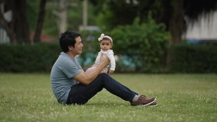 Wall Mural - happy father sitting and kissing his infand baby on a green grass filed  in the park