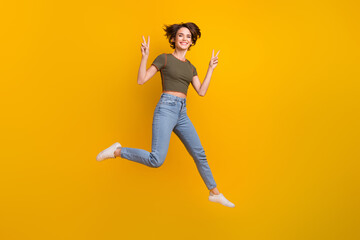 Wall Mural - Full length photo of cute adorable girl dressed khaki top jumping high showing two v-signs isolated yellow color background