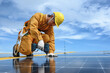 © kokliang1981 - Technician Young Wearing Safety Protective Clothing on Walkway and Using Tool Installing Solar Panel or Photovoltaic at Support Point in Daytime on Factory Roof Buildings.