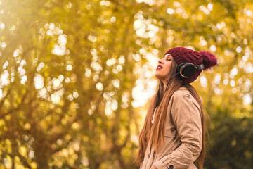 Portrait of a woman in autumn in a forest with brown leaves with her eyes closed listening to music with headphones