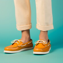 legs and feet wearing tan leather boat shoes and rolled up trousers isolated on plain blue studio background, made with generative ai
