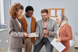 © Seventyfour - Group of young multicultural economists or analysts discussing data in financial documents at meeting while standing in front of camera