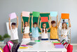 © Studio Romantic - Cheerful school children standing in row in classroom and holding different colorful mockup banners. Team of happy primary junior students play games, study new words and raise text copy space posters